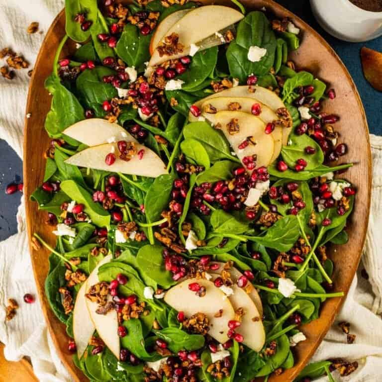 spinach salad on a brown wooden tray topped with pears, pomegranate, gorgonzola and pecans
