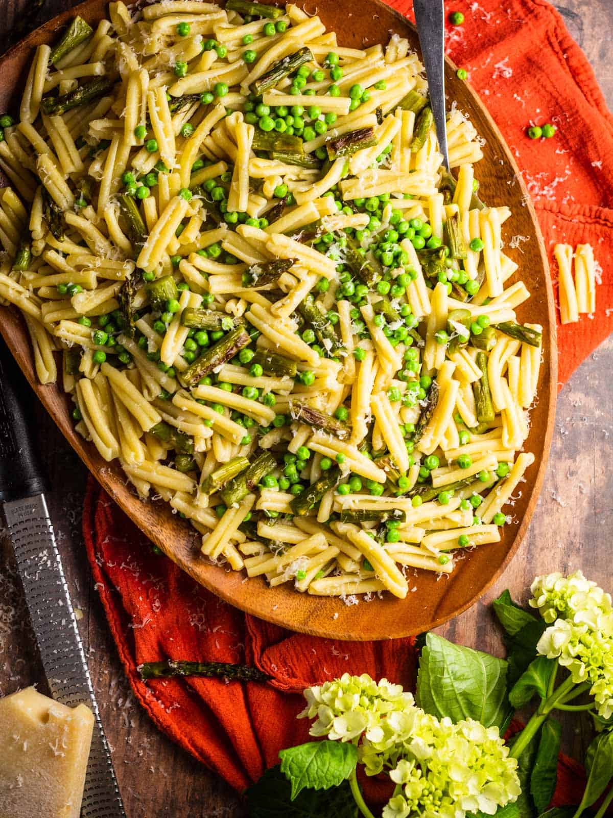 casarecce pasta with asparagus and peas on a wooden tray with block of cheese and flowers