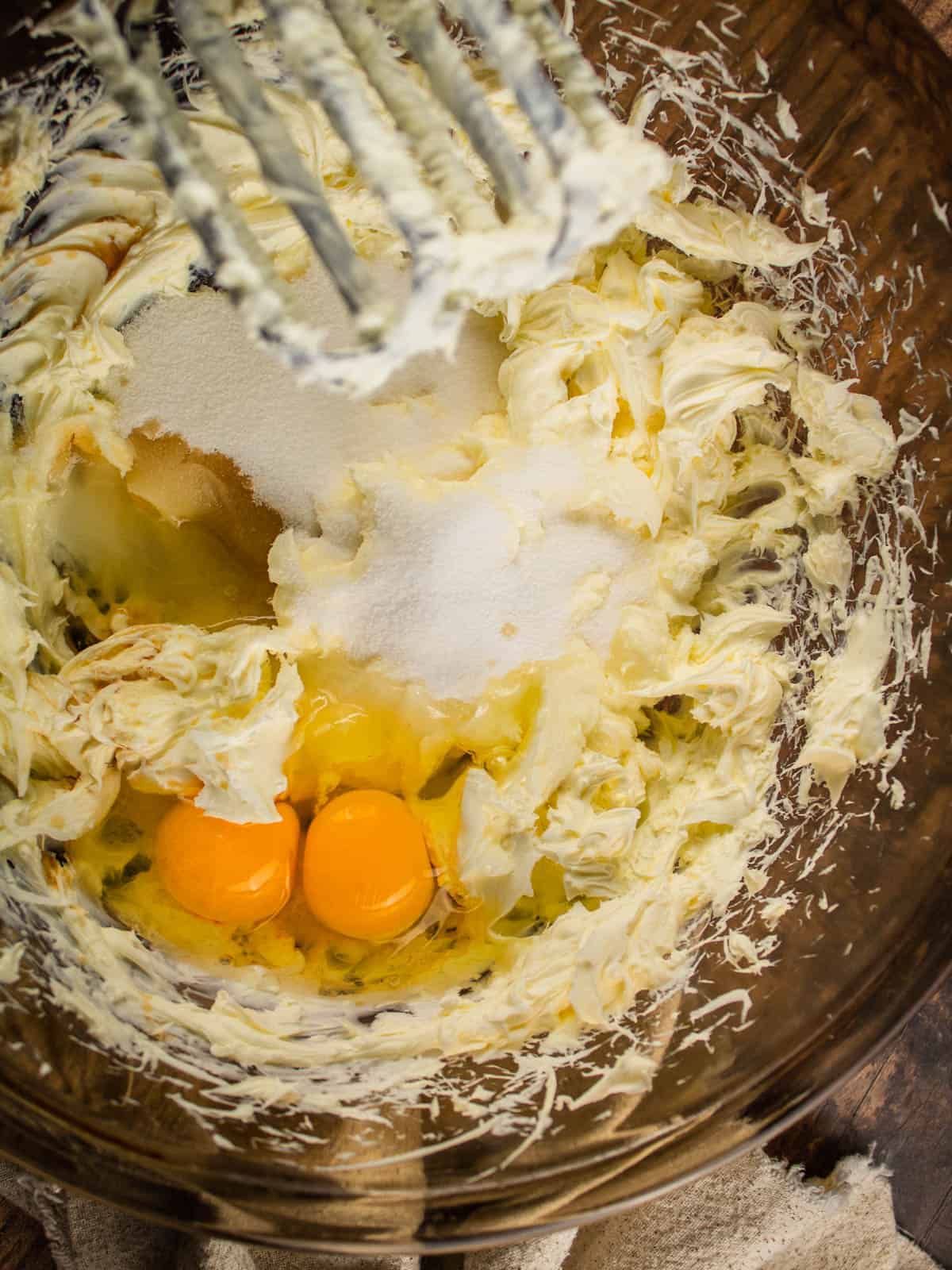 eggs and sugar with cream cheese in a mixing bowl