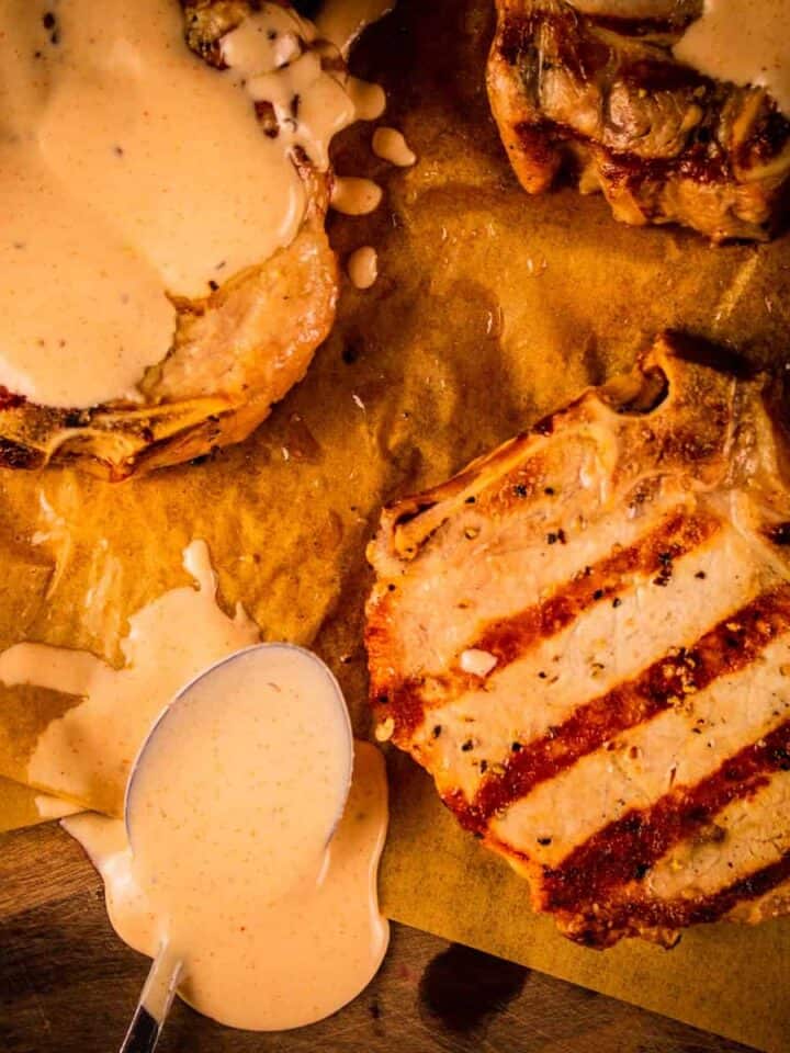 three grilled pork chops with two of them covered in white bbq sauce
