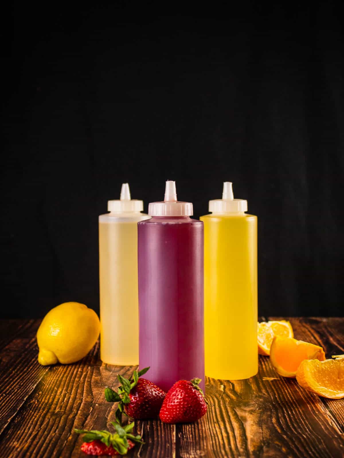 red, yellow and orange simple syrups in a squeeze bottles next to fresh fruit