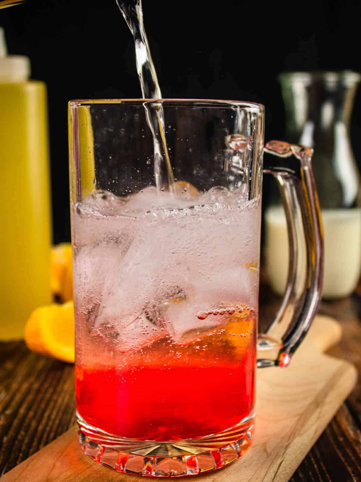 club soda pouring into a clear glass mug with ice and strawberry simple syrup
