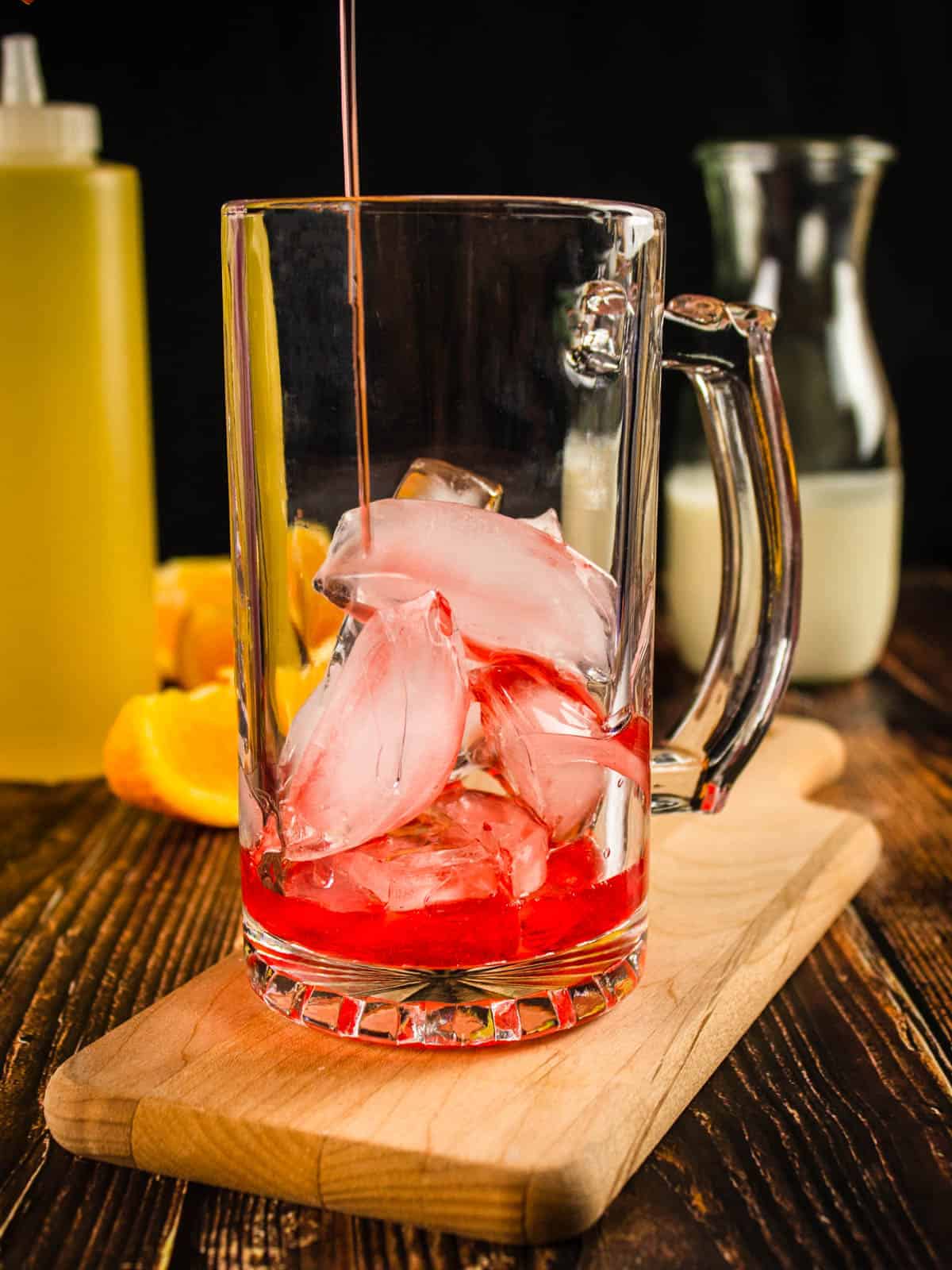 red simple syrup pouring into a glass mug with ice