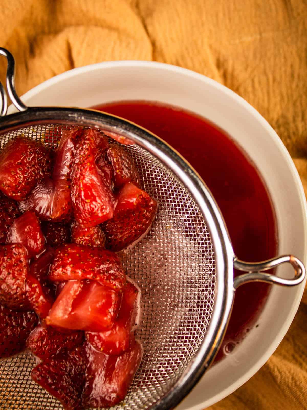 strainer filled with strawberries over a white bowl of red liquid