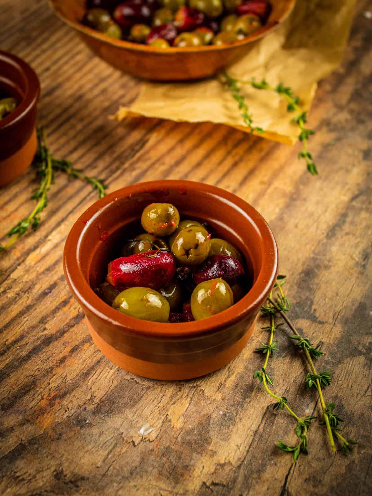 brown ceramic dish of roasted olives and grapes with a thyme sprig