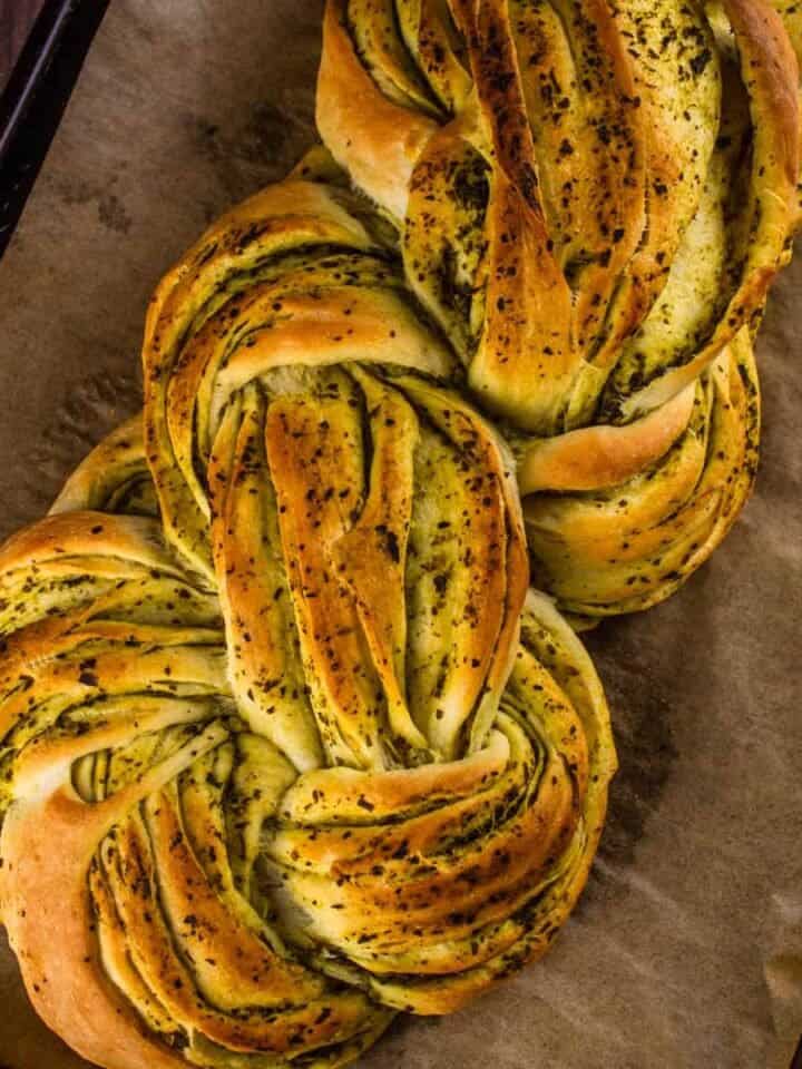 braided italian pesto bread with pesto on a sheet pan with parchment paper.