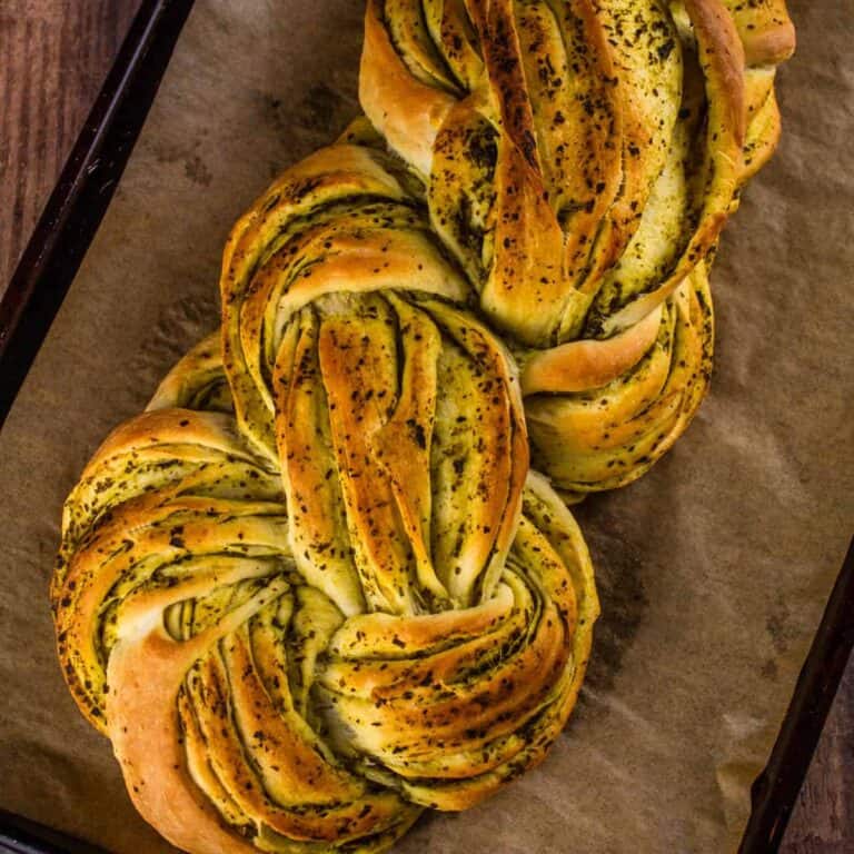 braided italian pesto bread with pesto on a sheet pan with parchment paper.
