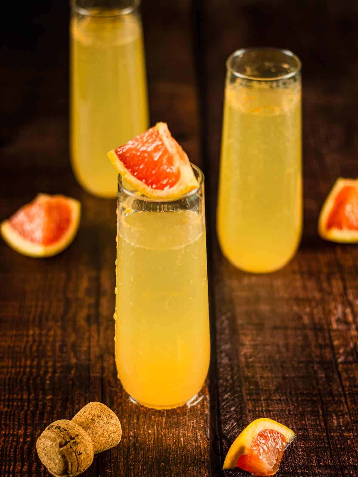 three stemless champagne flutes with grapefruit cocktail and grapefruit wedges