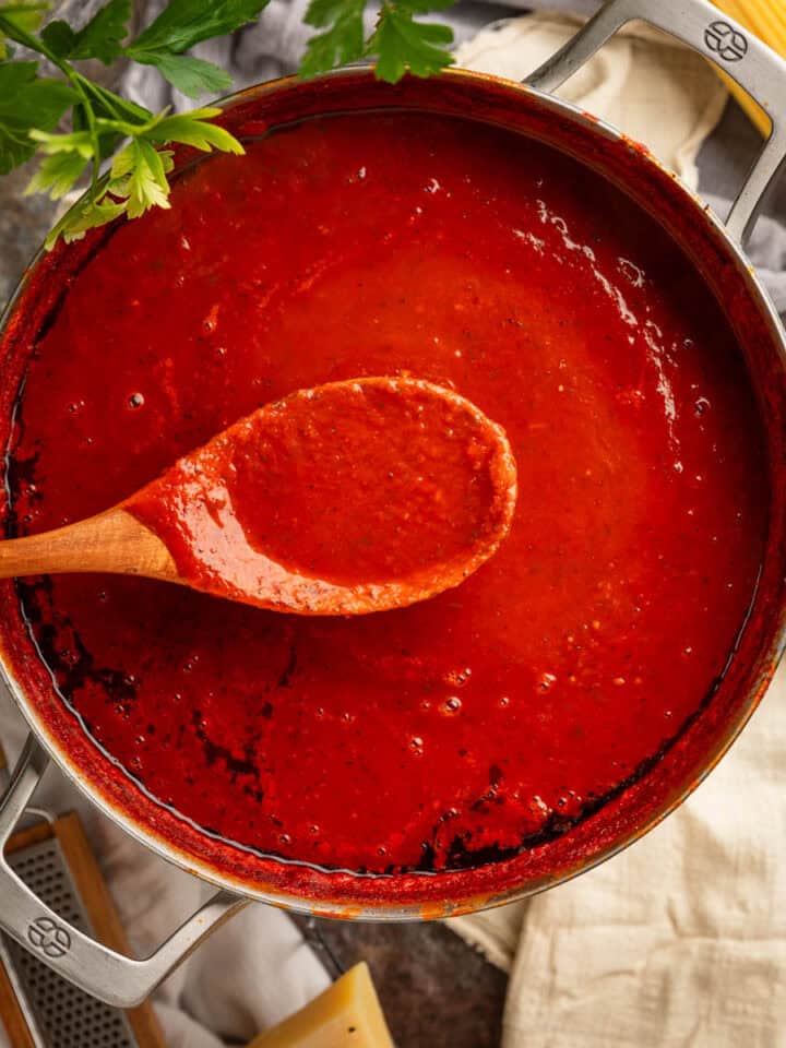 Wooden spoon holding red sauce over a large pot of sauce.