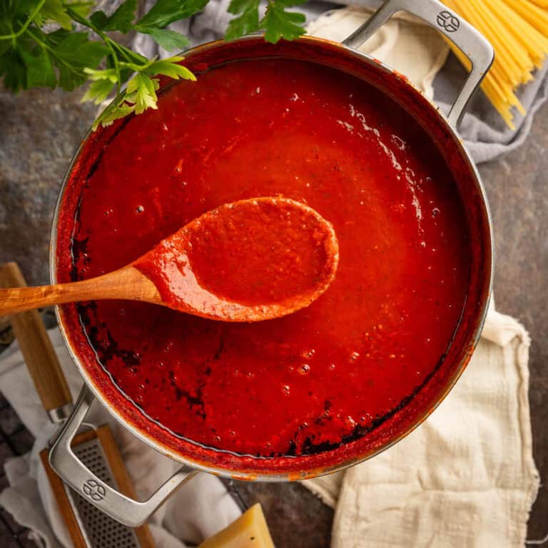 Wooden spoon holding red sauce over a large pot of sauce.