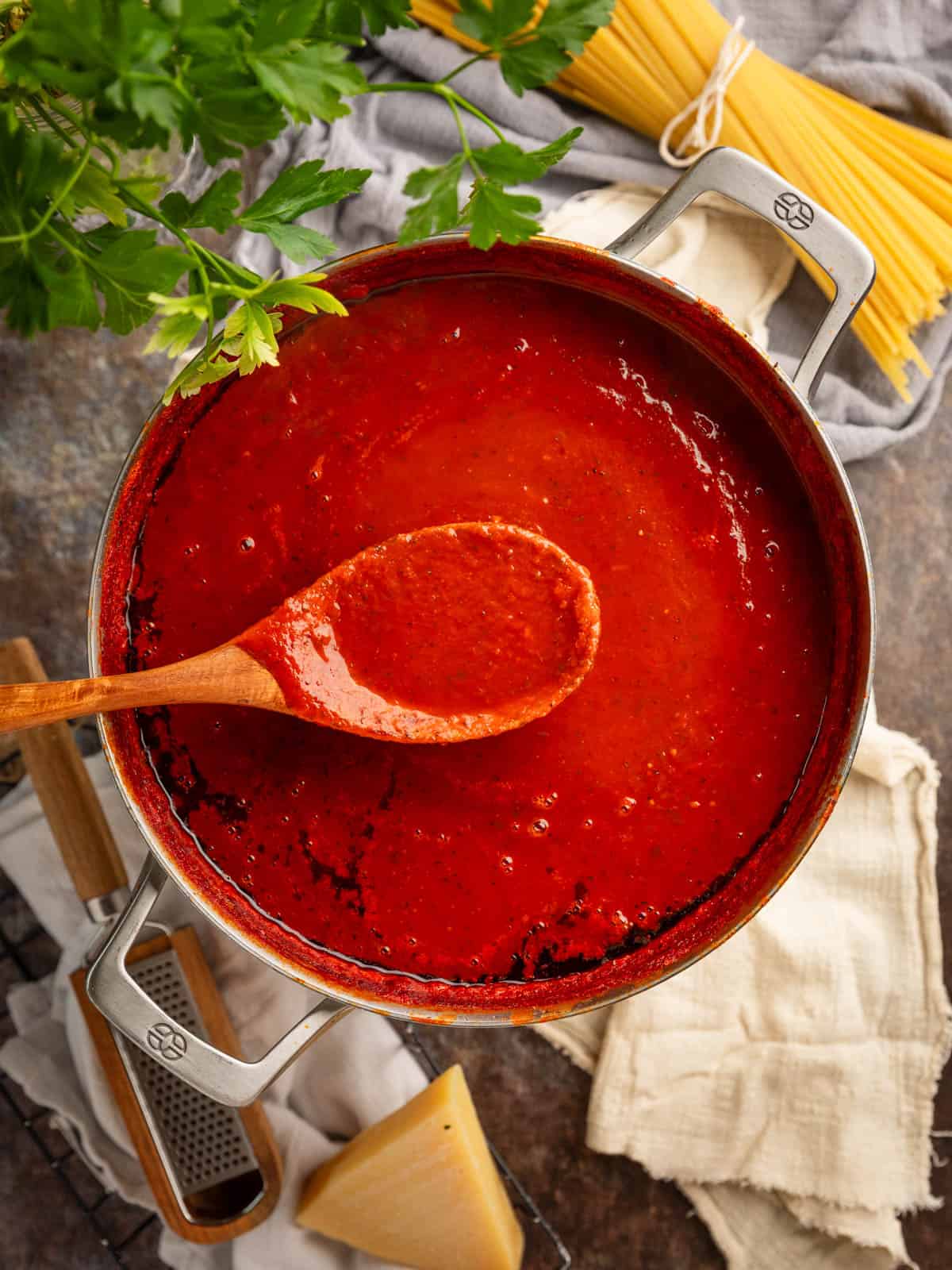 Large pot of red sauce with a wooden spoon holding some sauce over it.