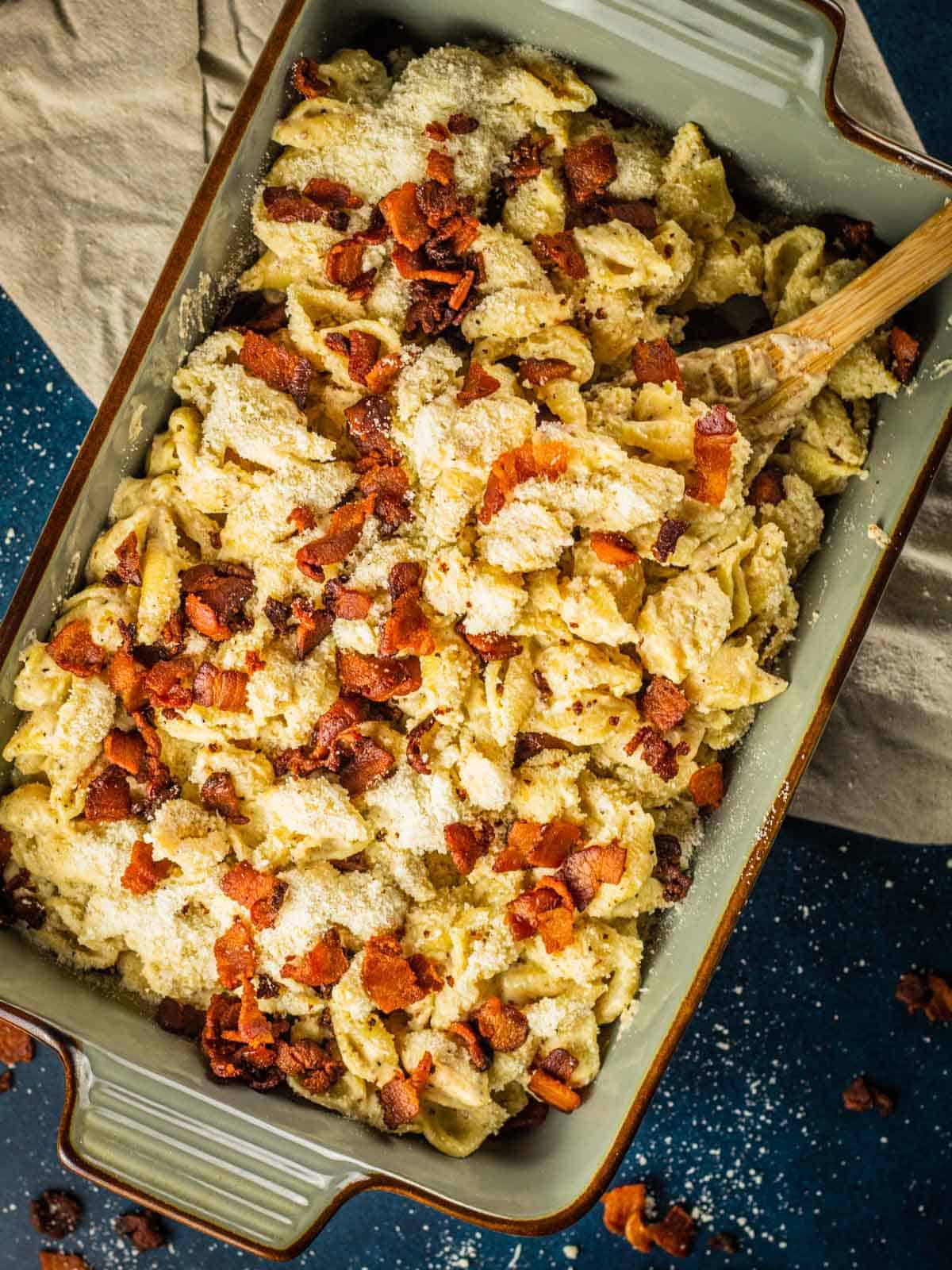 rectangle ceramic dish of shell pasta with creamy white sauce, crispy bacon pieces and grated parmesan