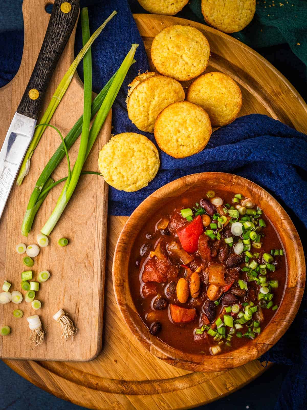 bowl of chili topped with sliced green onions next to corn muffins and sliced green onions
