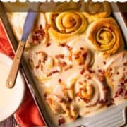 partially frosted cinnamon rolls with bacon on top.