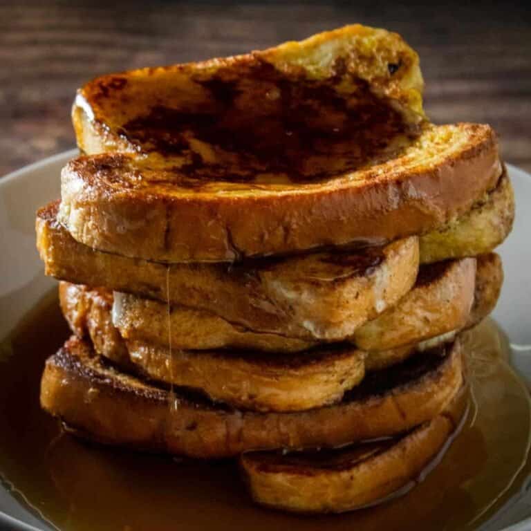 stack of french toast on a white plate covered in maple syrup.