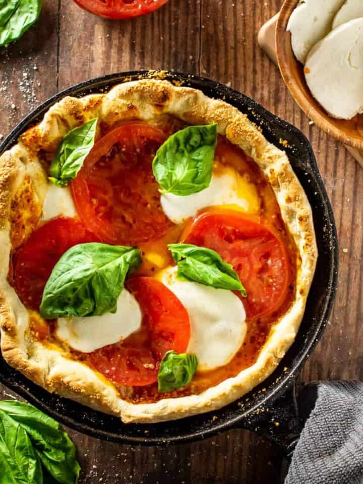 pizza in a cast iron skillet with tomatoes, cheese and fresh basil.