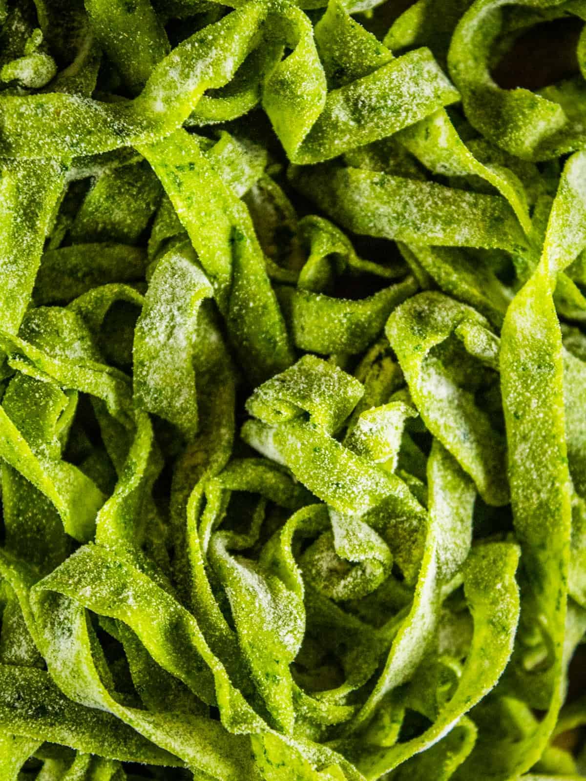 close up image fresh uncooked spinach fettuccine noodles dusted in flour