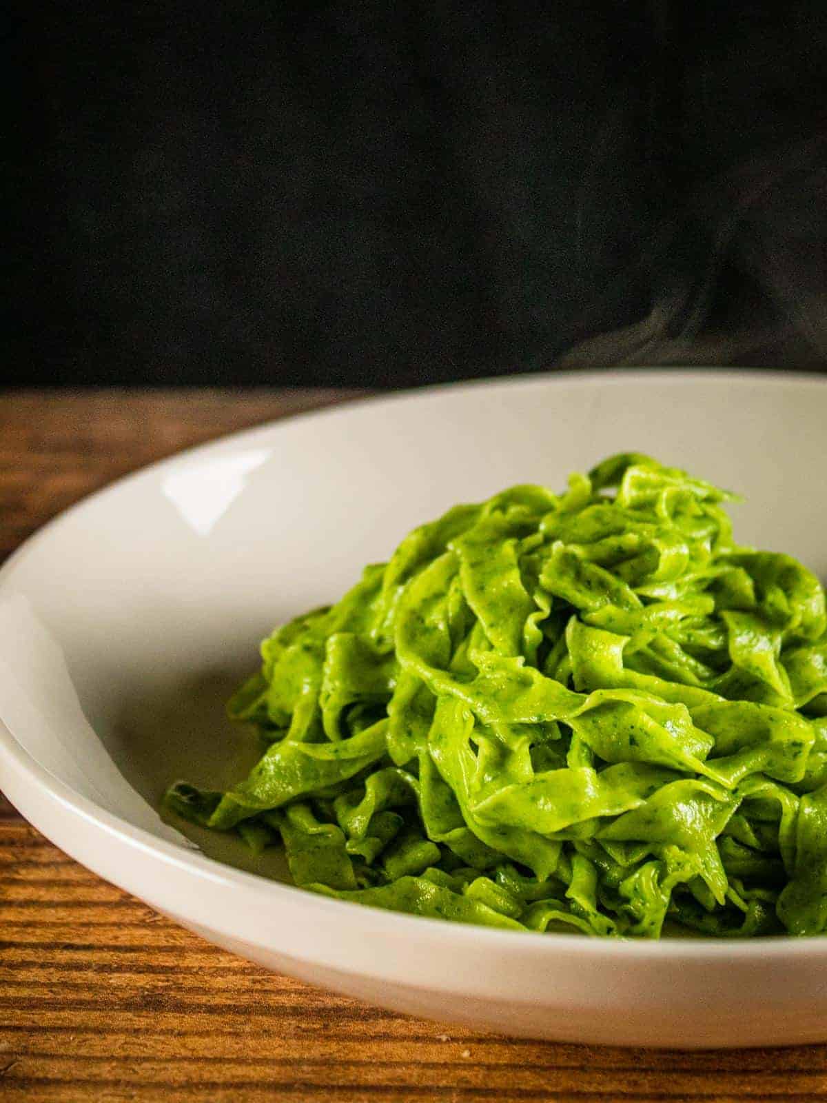 freshly cooked spinach fettuccine on a white plate with steam rising from it