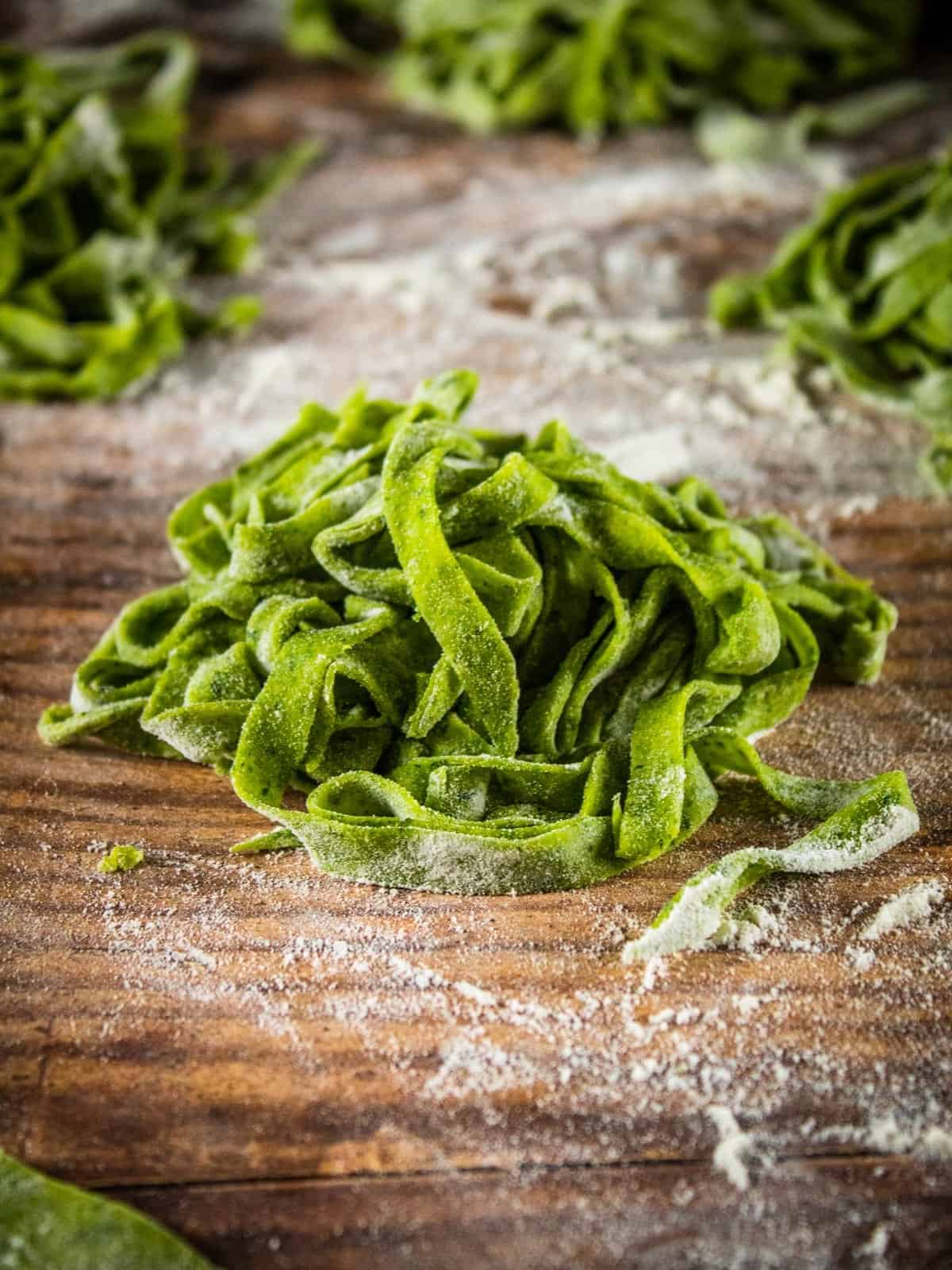 piles of uncooked spinach fettuccine pasta on a floured table.