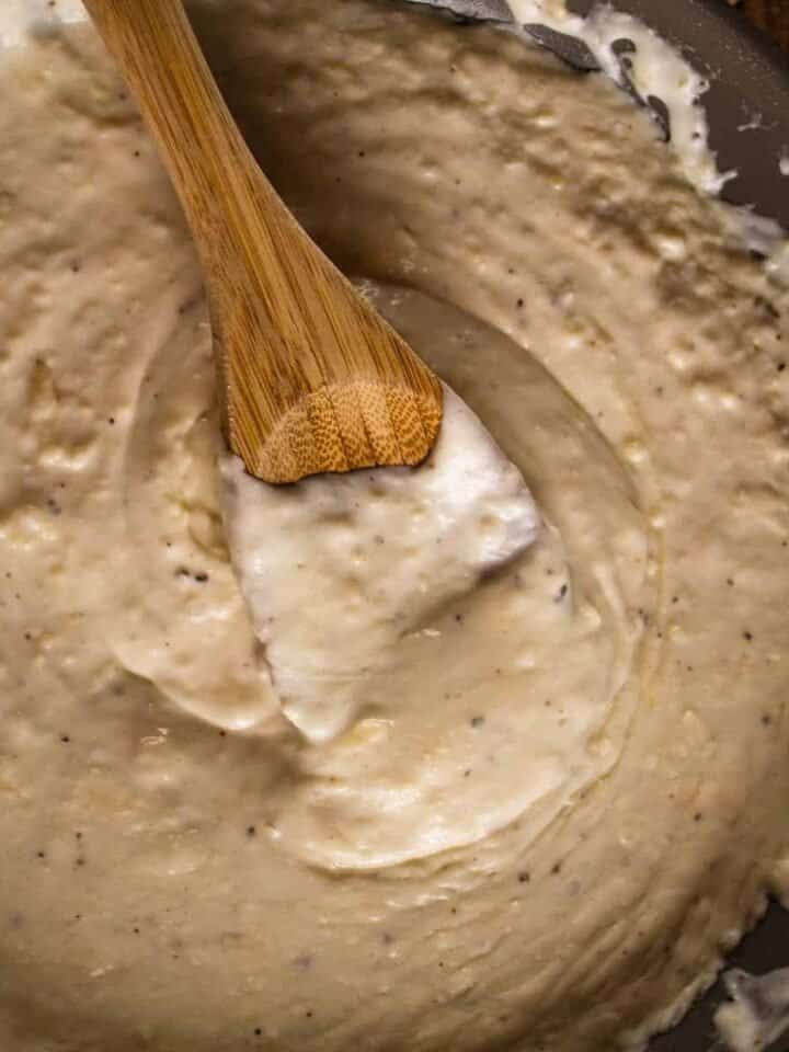 wooden spoon mixing an alfredo sauce in a pan.