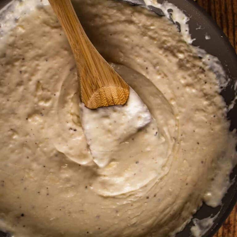 wooden spoon mixing an alfredo sauce in a pan.