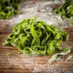 pile of uncooked homemade spinach fettuccine on a table