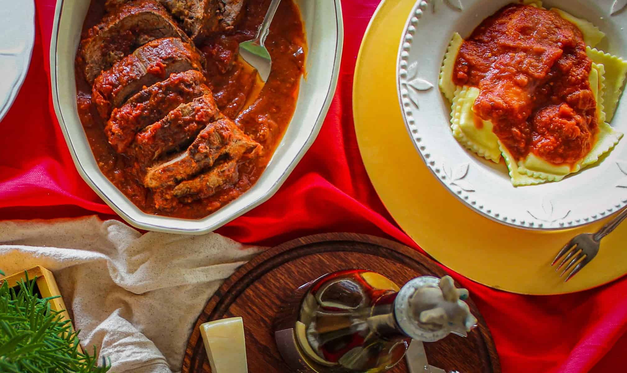 overhead shot of a dinner table with braciole and ravioli with marinara
