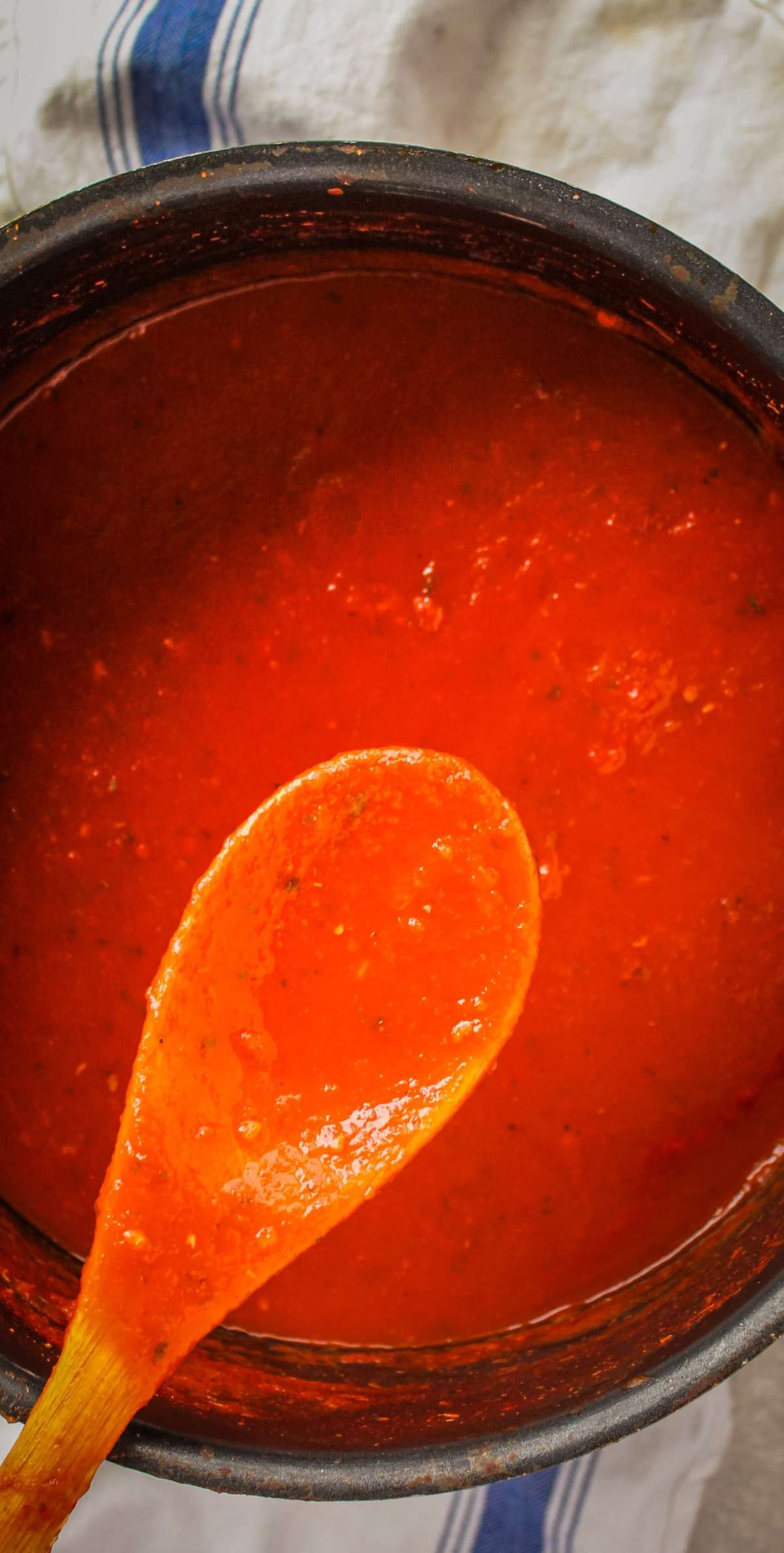 wooden spoon holding marinara sauce of a large pot of red sauce