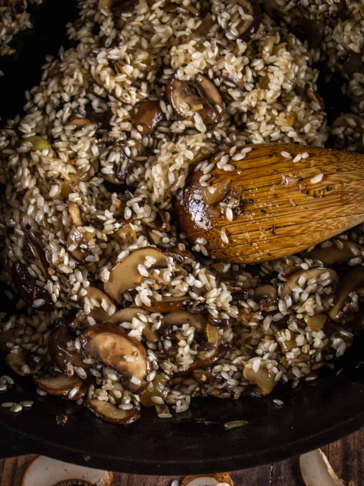wooden spoon stirring rice and mushrooms 