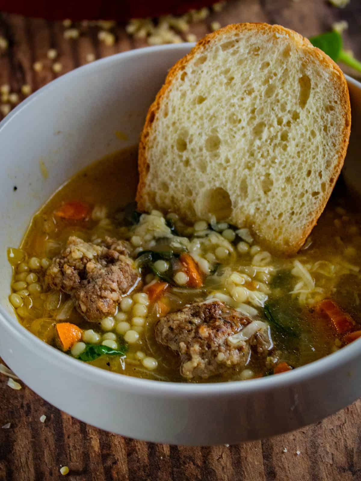 slice of french bread in a bowl of italian wedding soup with meatballs.