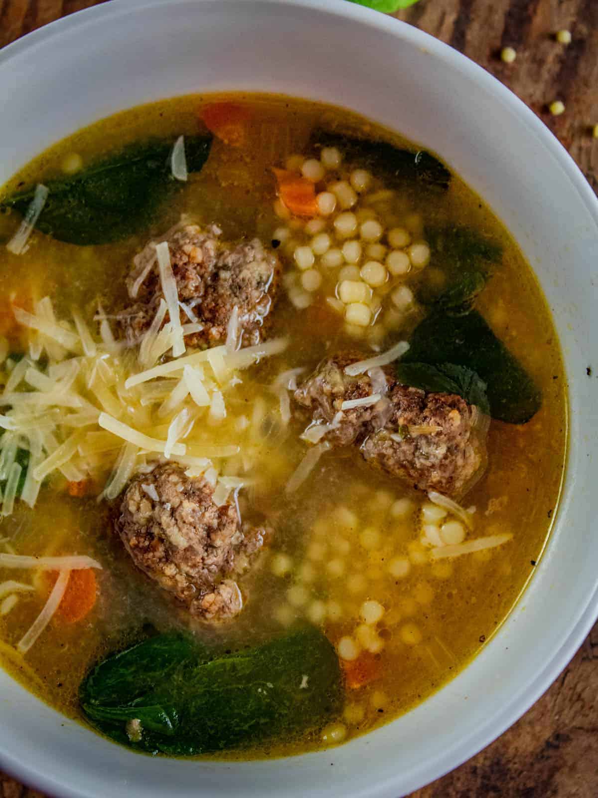 italian wedding soup with meatballs and acini de pepe in a white bowl topped with parmesan.