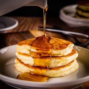 stack of three pancakes on a plate with syrup pouring over them.