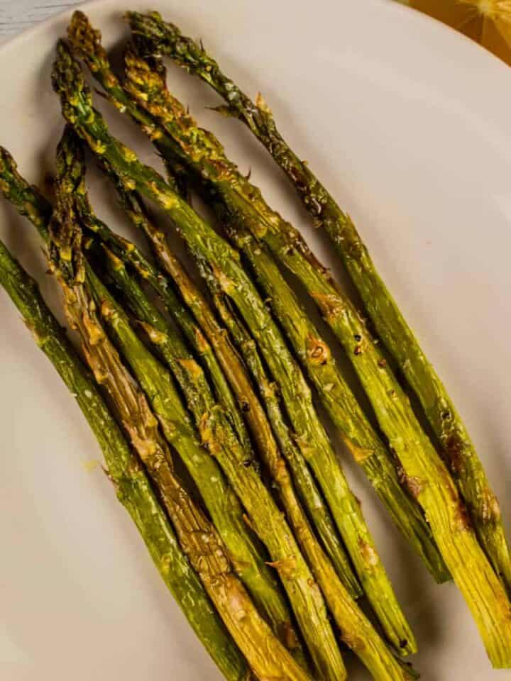 roasted asparagus on a white plate with a lemon on the side