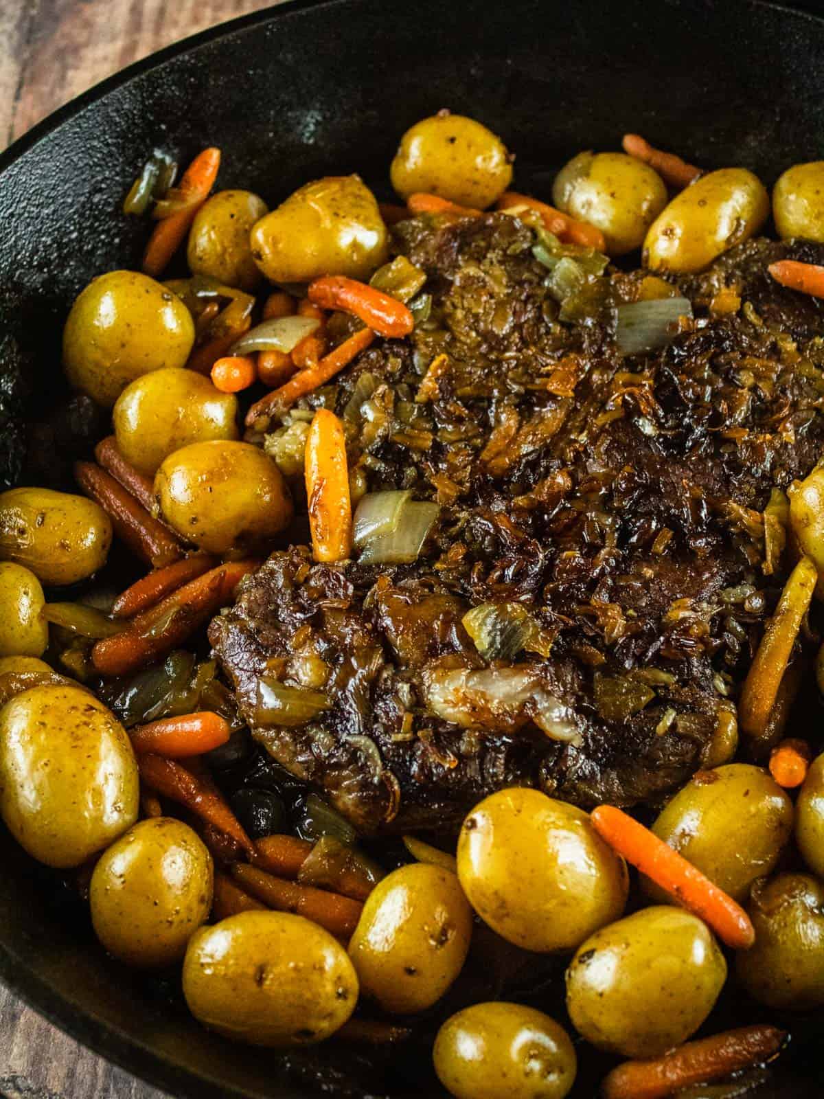 cook pot roast with yellow potatoes, baby carrots and sliced onions in a cast iron skillet.