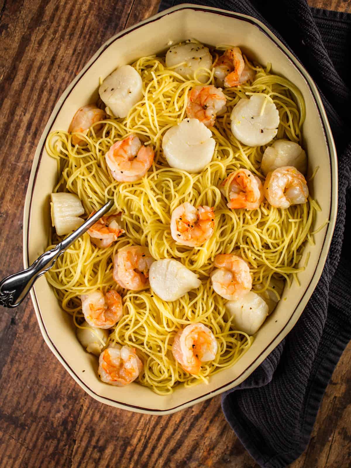 ceramic oval dish with roasted shrimp and scallops over angel hair pasta on a wooden table