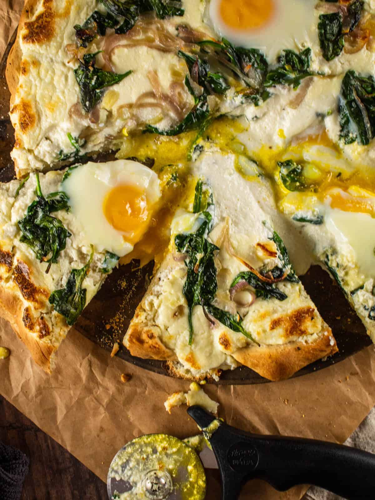 close up shot of partially sliced breakfast pizza with eggs, spinach, red onion and ricotta cheese