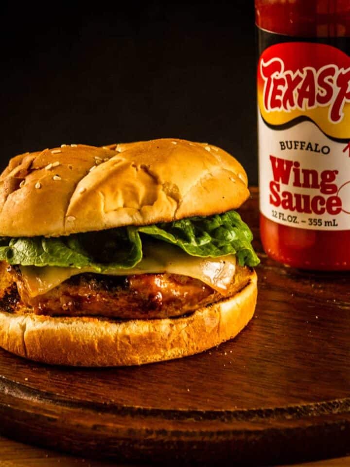 burger on a wooden tray next to a bottle of wing sauce