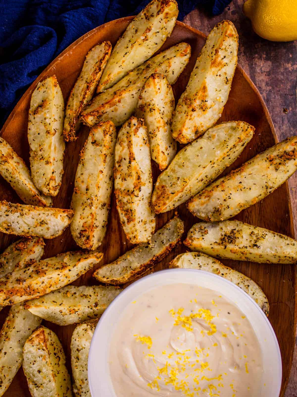 roasted potato wedges on a wooden tray with a bowl of dip