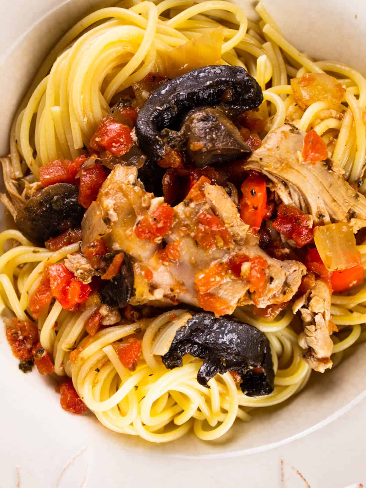 chicken with mushrooms, peppers, onions and tomatoes on spaghetti in a bowl.