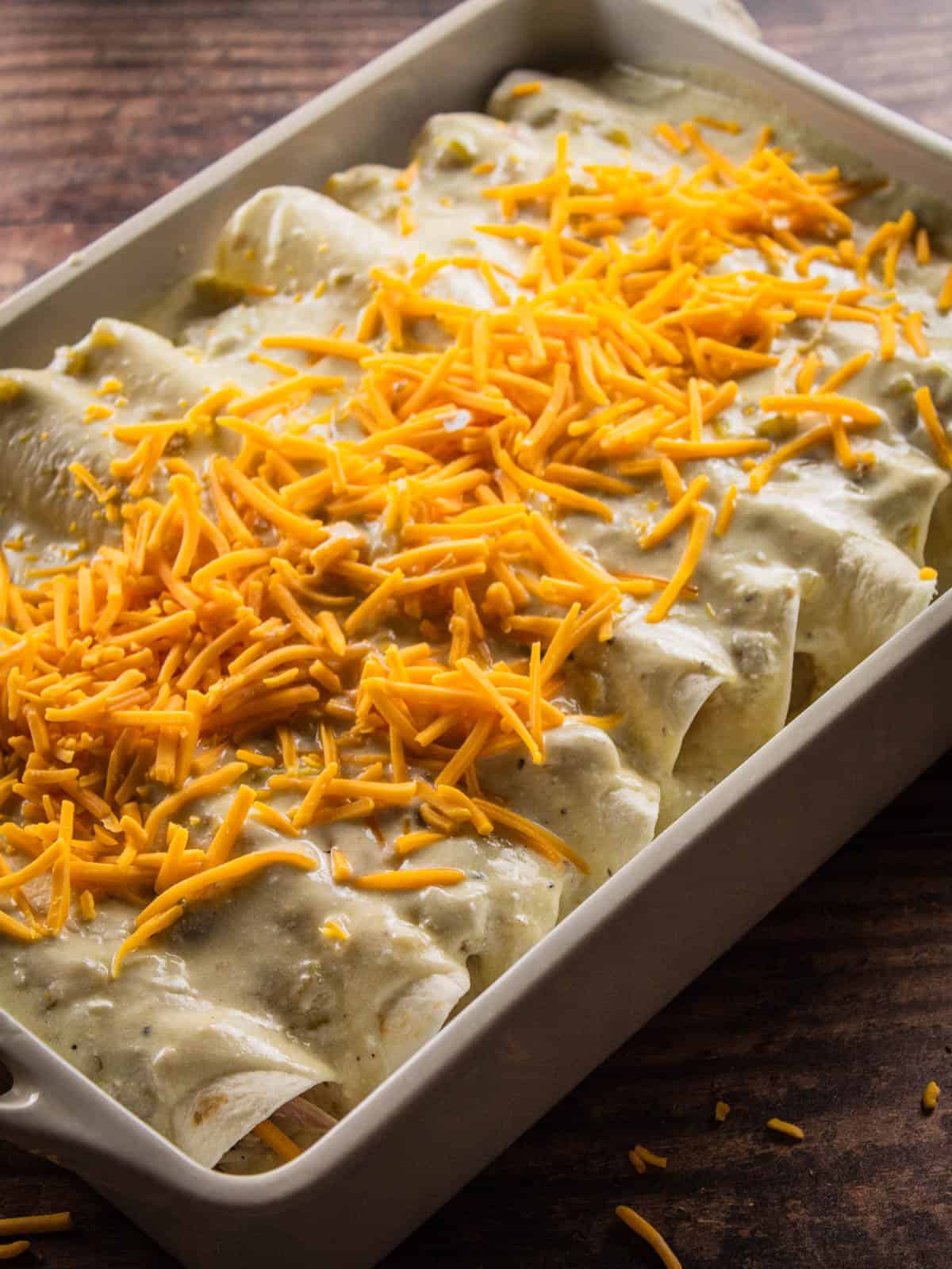 enchiladas topped with sauce and cheese before baking