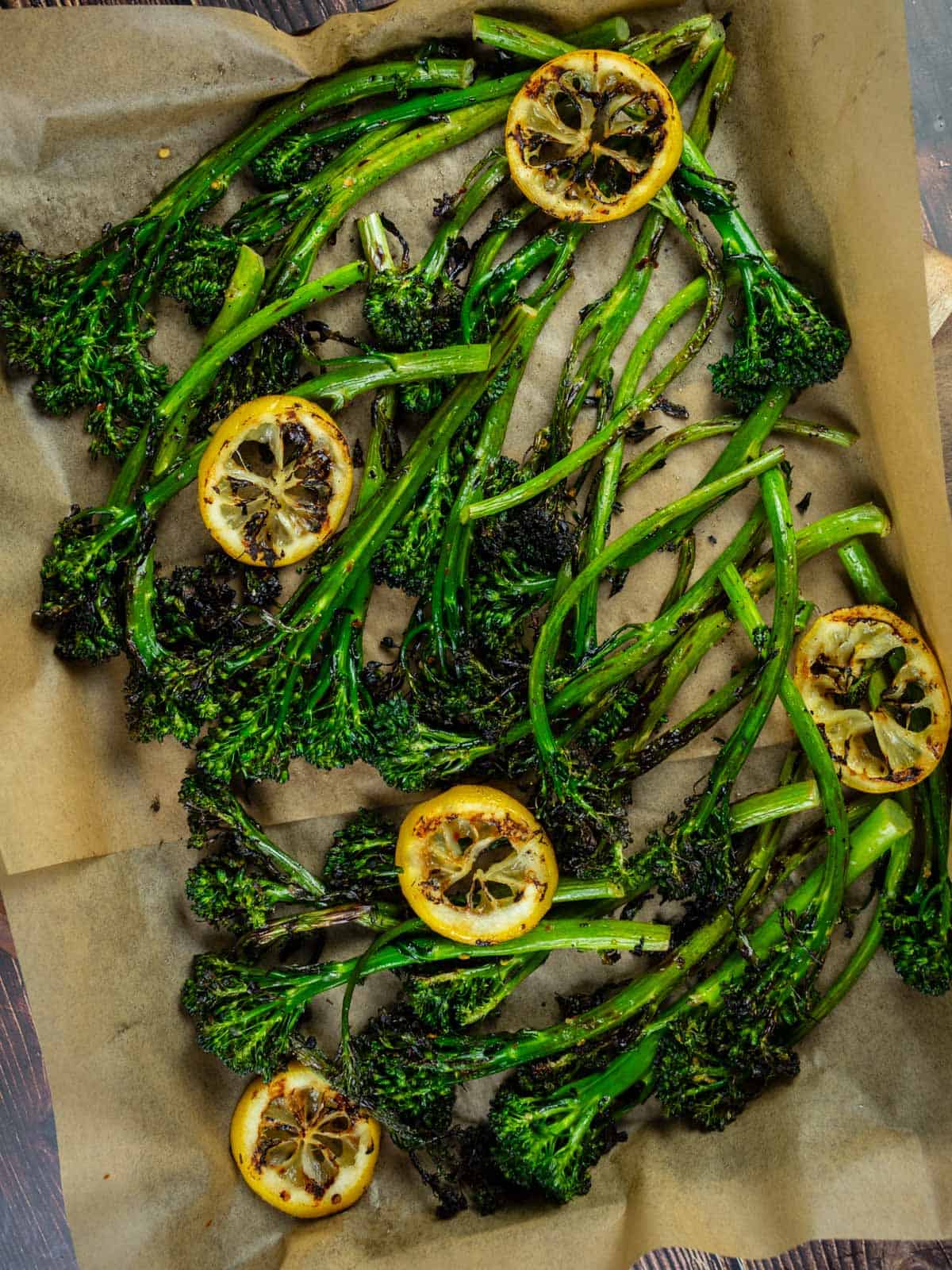 grilled broccolini with grilled lemon slices on a sheet pan lined with parchment paper.