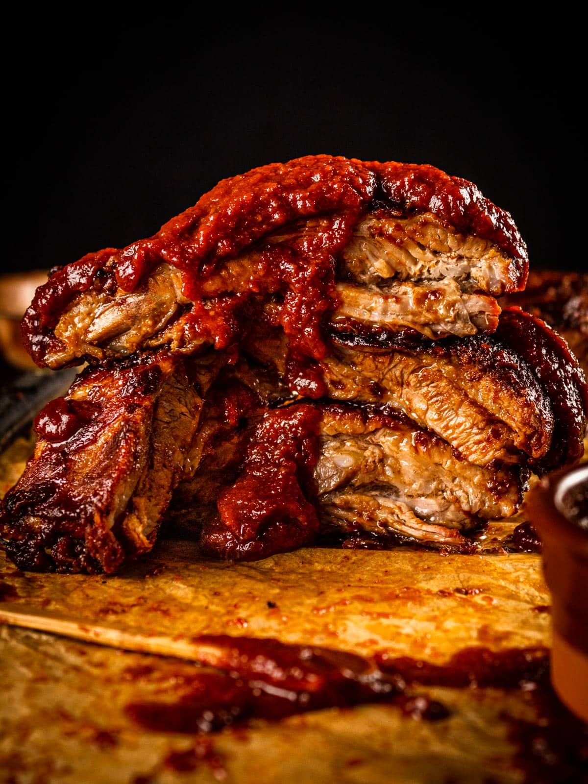cut ribs stacked on each other with barbecue sauce dripping over the top of them.