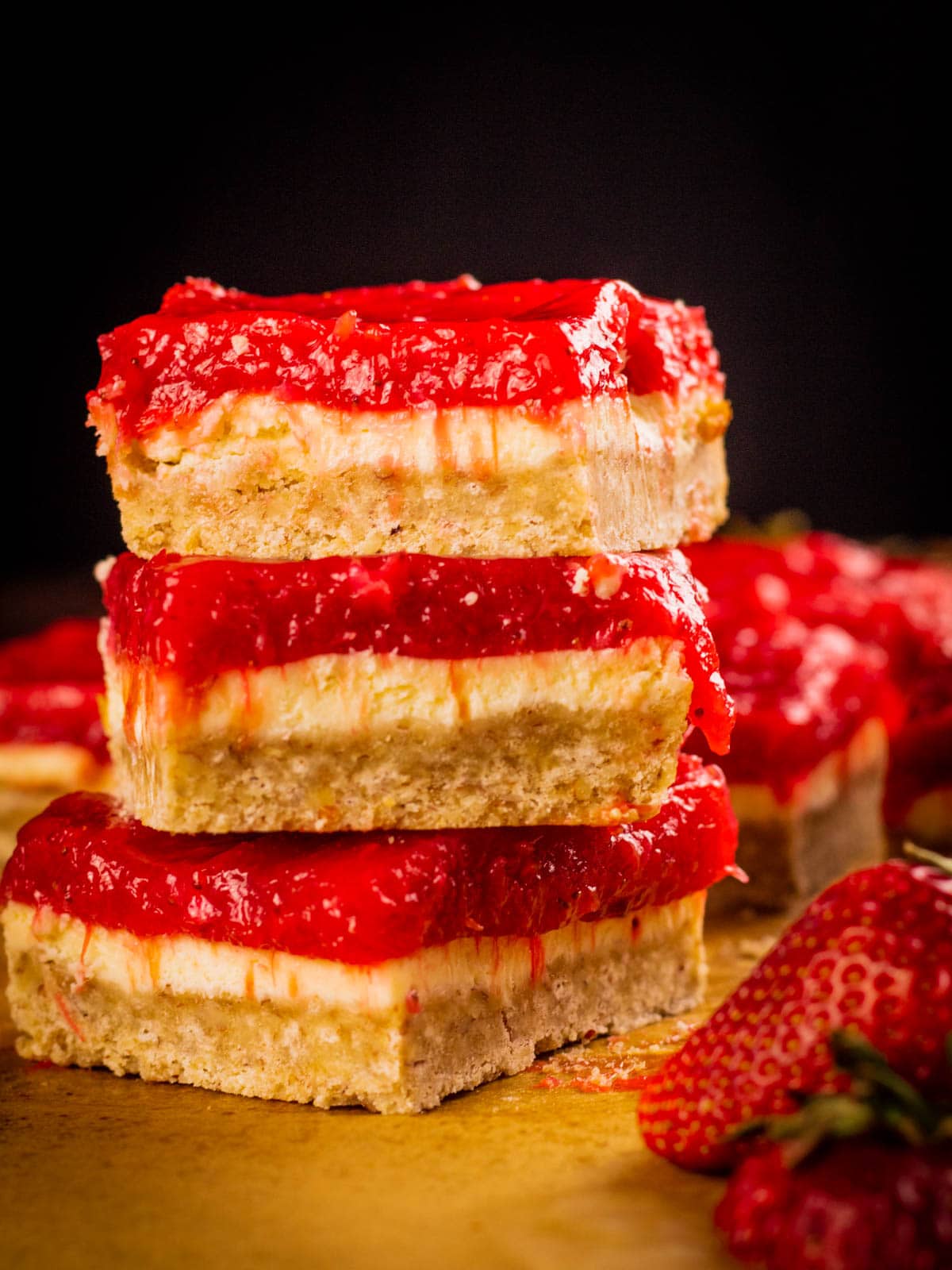 stack of strawberry rhubarb cheesecake bars next to fresh strawberries