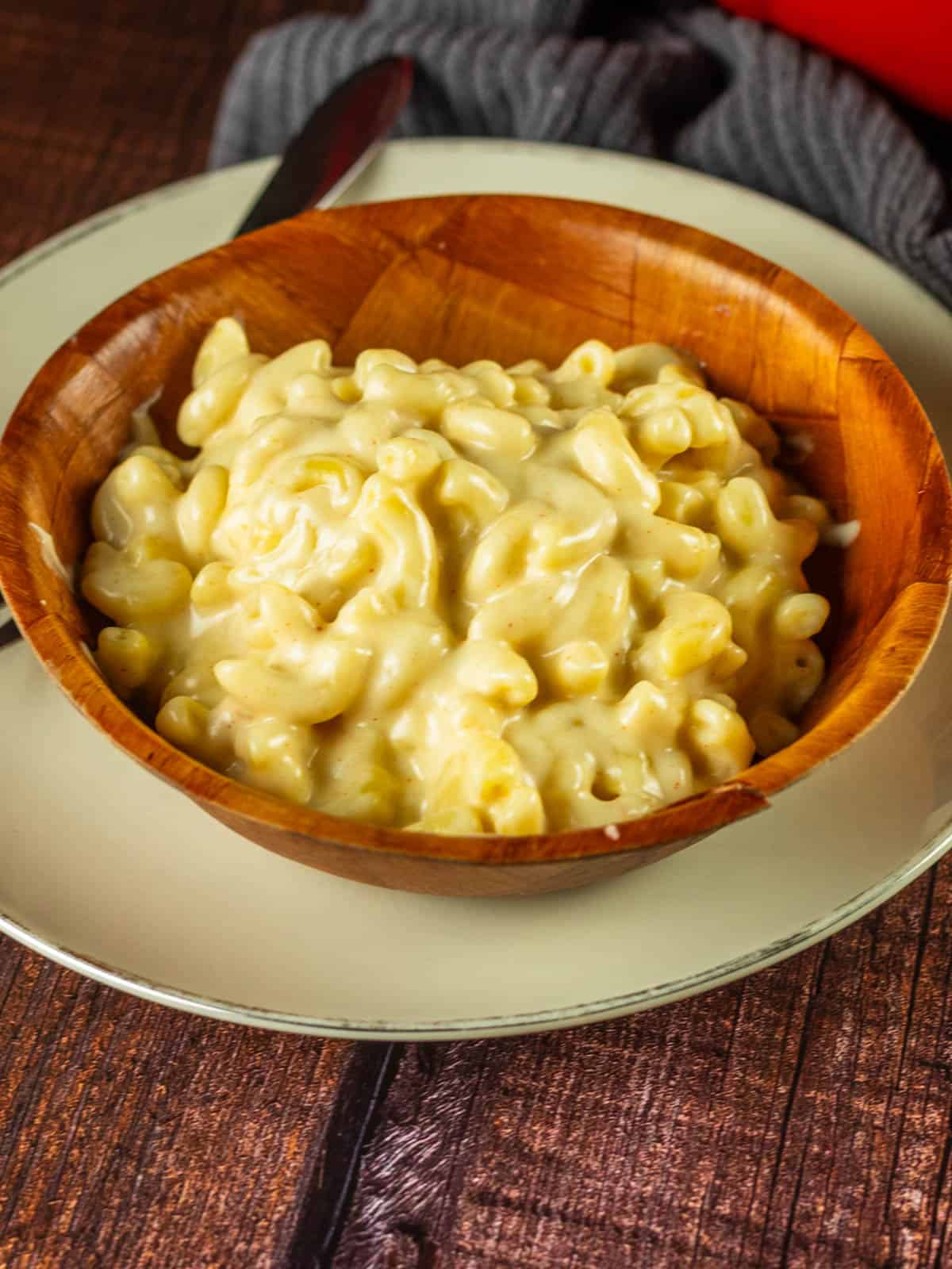 wooden bowl filled with white macaroni and cheese on a plate with a fork.