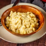 white mac and cheese in a wooden bowl on a plate with a fork.