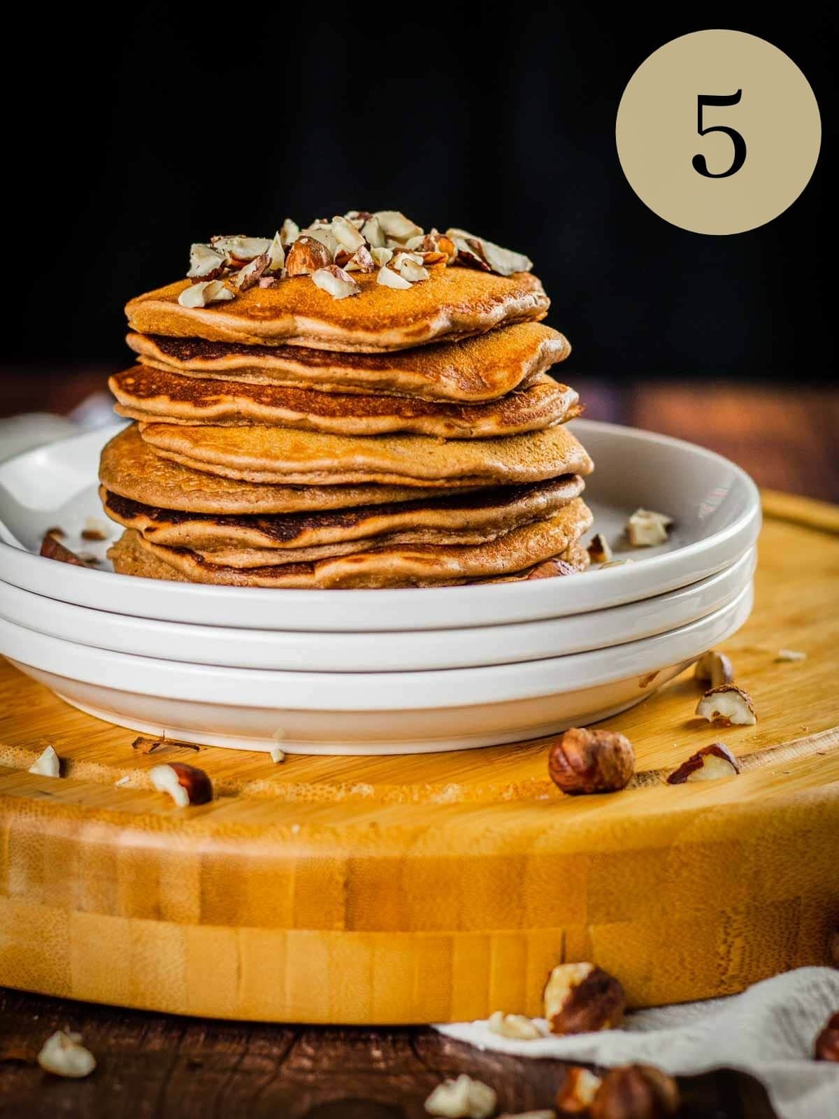 stack of nutella pancakes on a stack of white plates topped with chopped hazelnuts