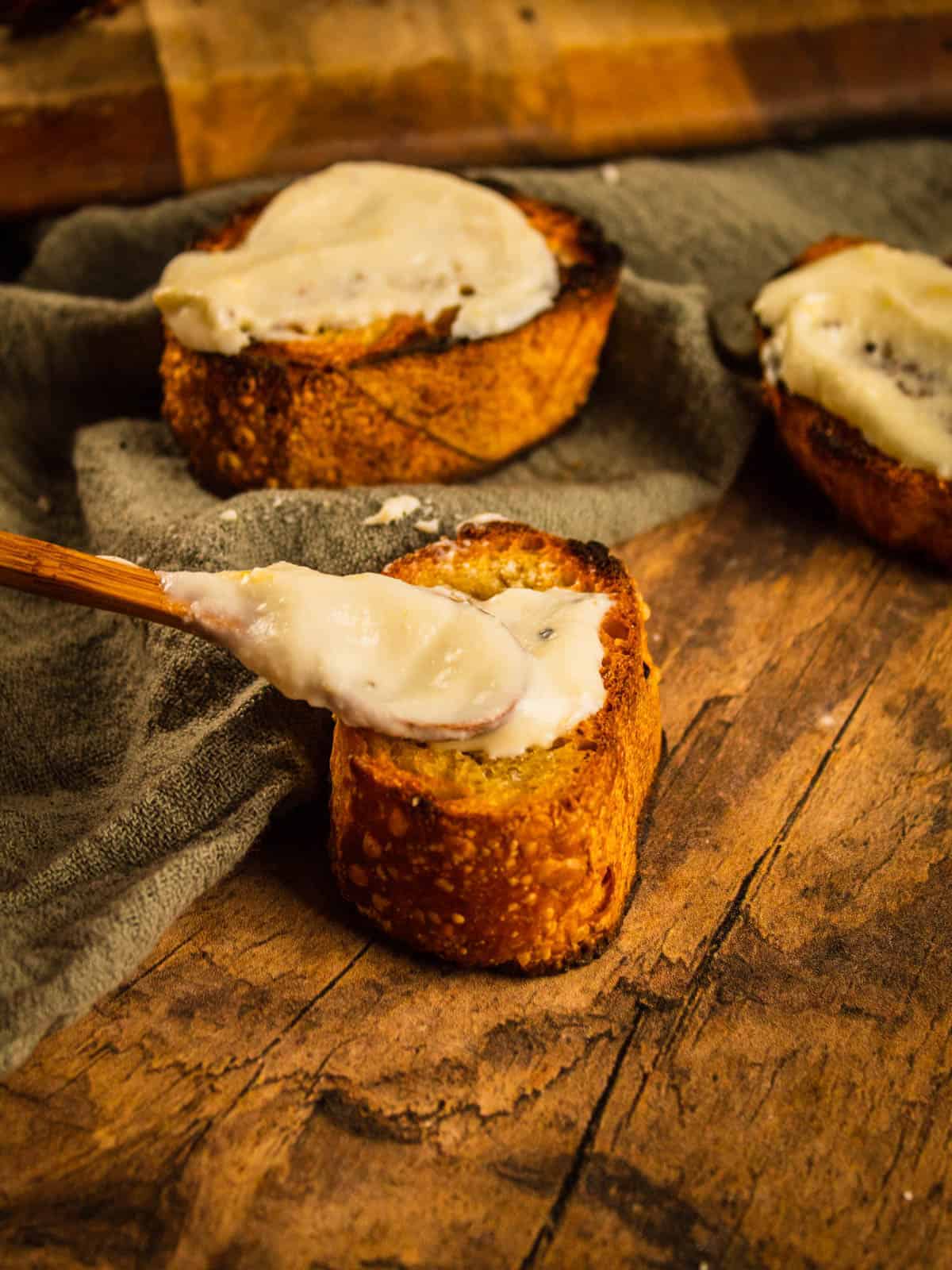 small wooden spoon dropping ricotta spread on baguette slice