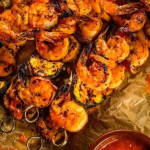 grilled shrimp and veggie skewers covered in sauce on parchment next to sauce.