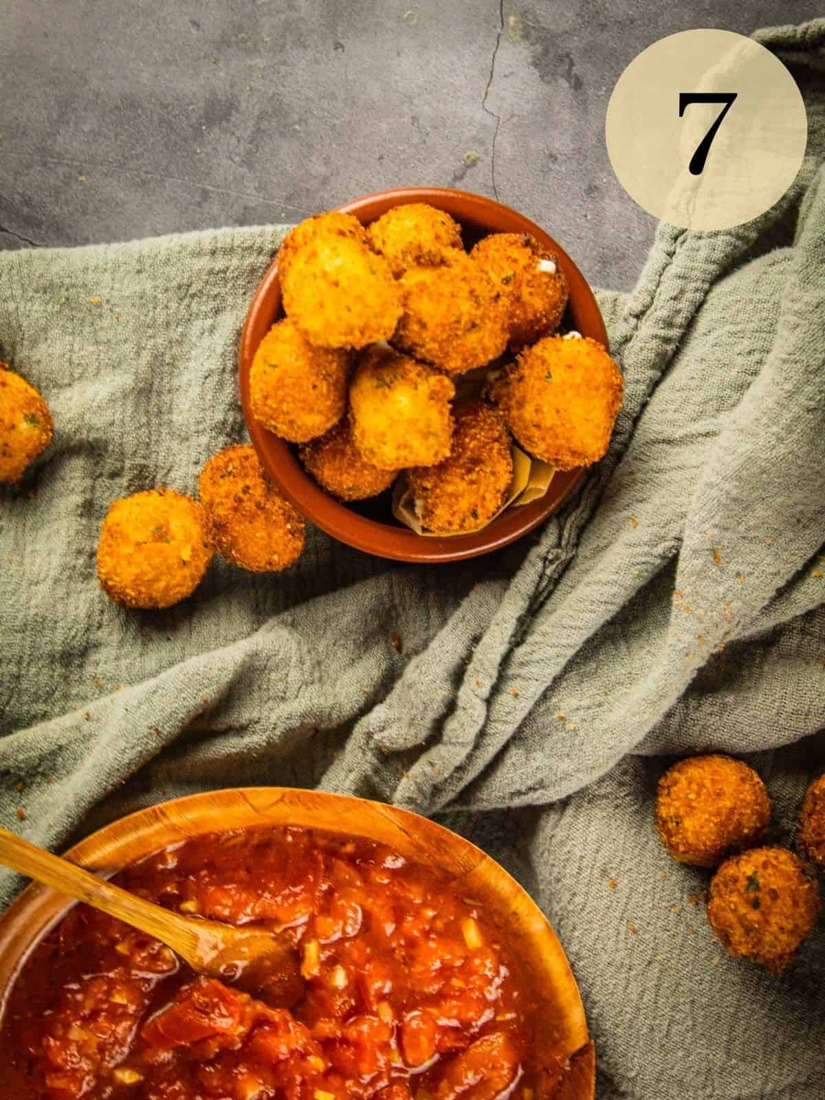 fried goat cheese balls in a small dish next to a bowl of arrabiata dipping sauce.