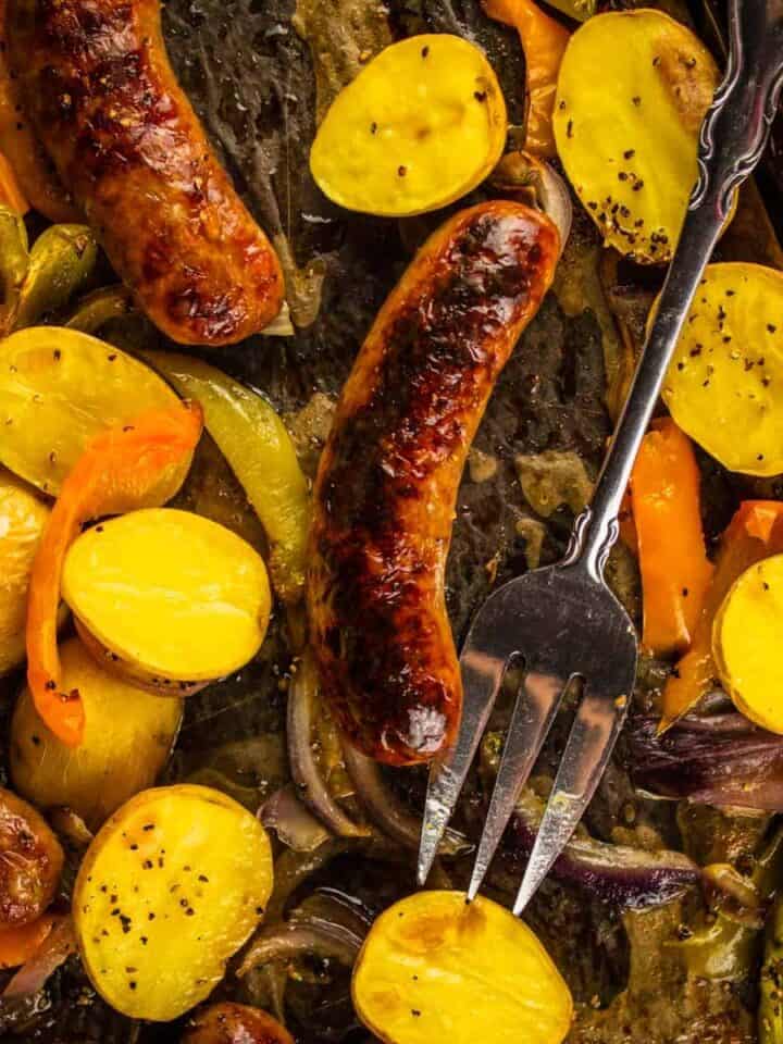 browned sausage on a sheet pan with halved potatoes and sliced peppers and onions